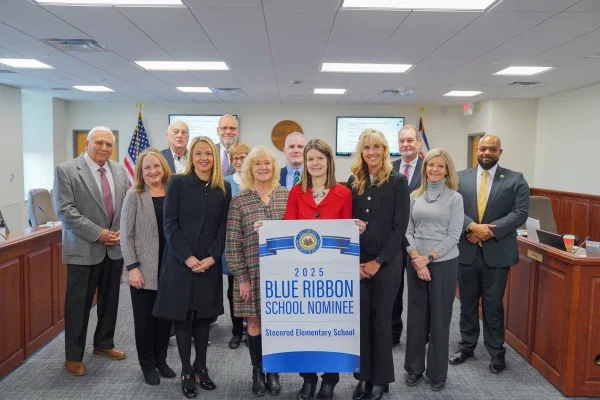 A group of people gathered around a banner with the words "2025 Blue Ribbon School Nominee Steenrod Elementary School" on it.