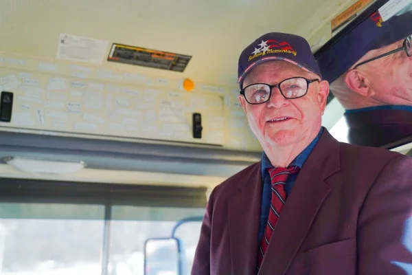 John Sitar smiling while standing beside the driver's seat on a school bus.