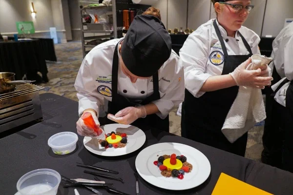 A person adding a fruit drizzle to a dessert plate.