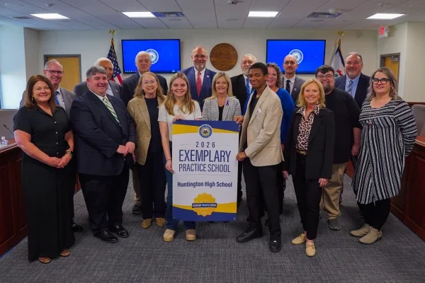 Members of Huntington High School and West Virginia Board of Education members smiling while holding an Exemplary Practice School banner.