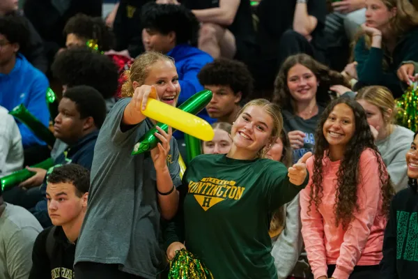 Two students smiling and pointing while other students smile behind them. 