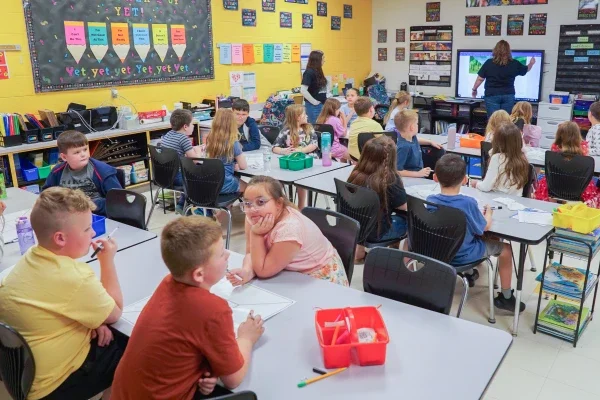 Students in elementary classroom listening to teacher instruction from front of classroom