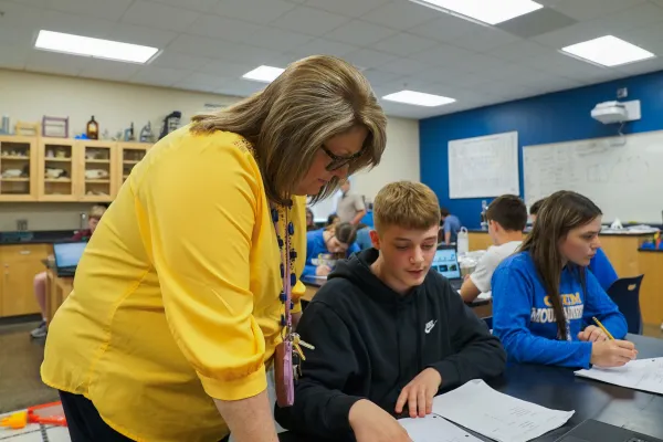 Female teacher assisting student in classroom.