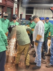 Students and an instructor watching another student weld something.