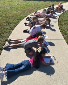 Student laying on the sidewalk observing shadows.