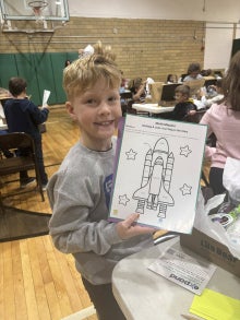 A student holding a math activity depicting a rocket ship.