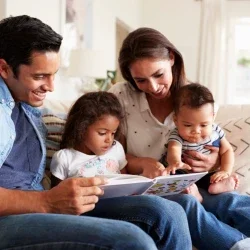 Young Hispanic family of four sitting on the sofa reading a book together in their living room
