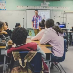 Class of students listening to their teacher speak.