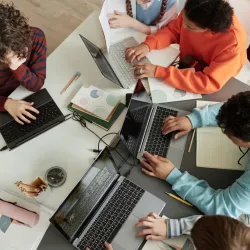Top view at diverse group of teen school children using computers in classroom studying together at table for Governor's School of Computer Science.