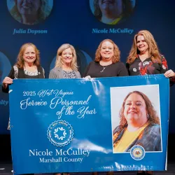 Pictured is Nicole McCulley posing for a group photo while holding a banner.
