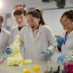 Students dressed in laboratory protective equipment watching an experiment with expanding foam