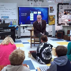 Teacher sitting on a chair in front of students in a classroom.