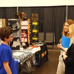 Young boy speaking to two women, project board in background.