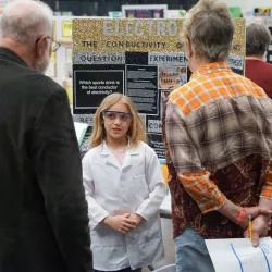 Young student showing off her science fair entry to two adult fair attendees