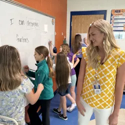 Female teacher smiling at students while they complete an activity.