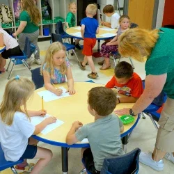 A woman assisting children with a classroom activity.