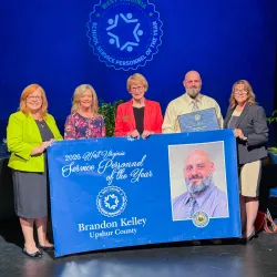Five people holding a banner. 2026 School Service Personnel of the Year Brandon Kelley.