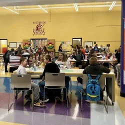 Students sitting at tables eating food inside of a school cafeteria.