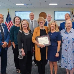 West Virginia Board of Education members surrounding Debra Sullivan. She is holding a frame.