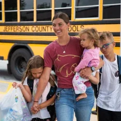 A family walking into school with a school bus behind them.