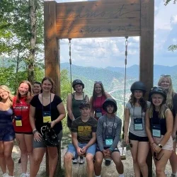 Students smiling and posing in front of a large wooden outdoor swing. 