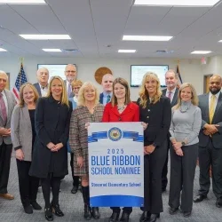 A group of people gathered around a banner with the words "2025 Blue Ribbon School Nominee Steenrod Elementary School" on it.