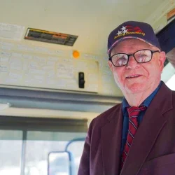 John Sitar smiling while standing beside the driver's seat on a school bus.