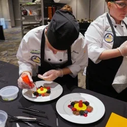 A person adding a fruit drizzle to a dessert plate.
