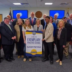 Members of Huntington High School and West Virginia Board of Education members smiling while holding an Exemplary Practice School banner.