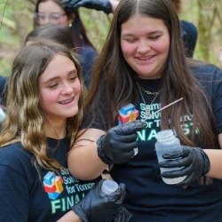 Two students smiling while looking at a bottle of water. 