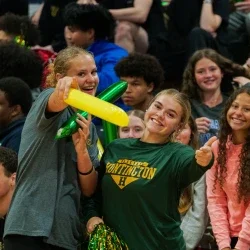 Two students smiling and pointing while other students smile behind them. 