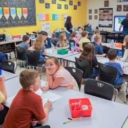 Students in elementary classroom listening to teacher instruction from front of classroom